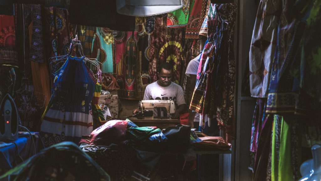 Man with sewing machine surrounded by colorful garments in Cape Verde