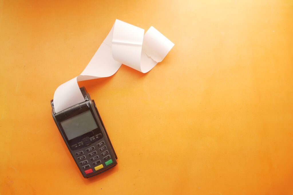 A payment terminal with receipt paper ejected on a yellow background.